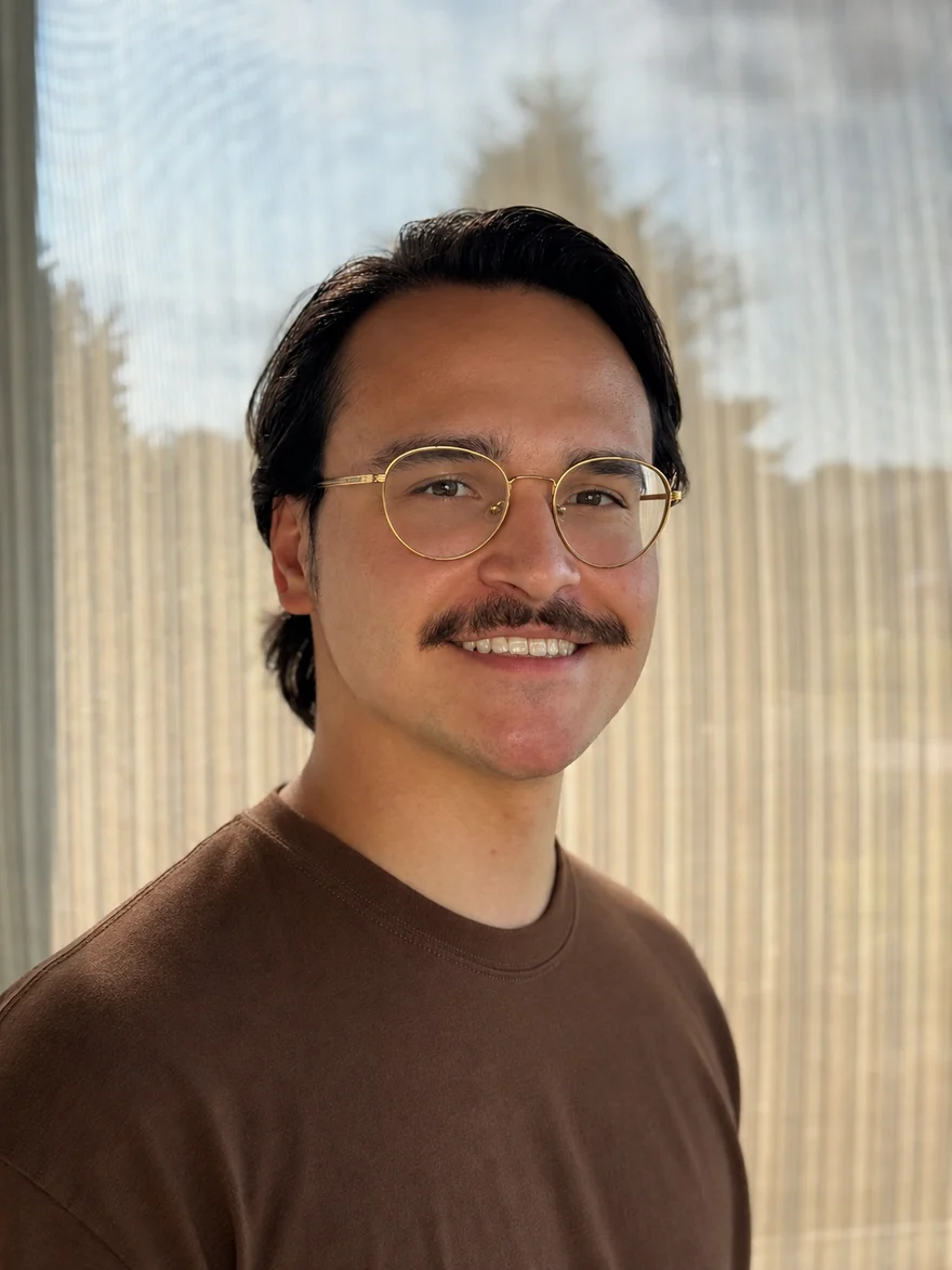 Felix Diez, founder of First Cause Studio, smiling in round gold-rimmed glasses, warm daylight coming through a curtained window behind him.